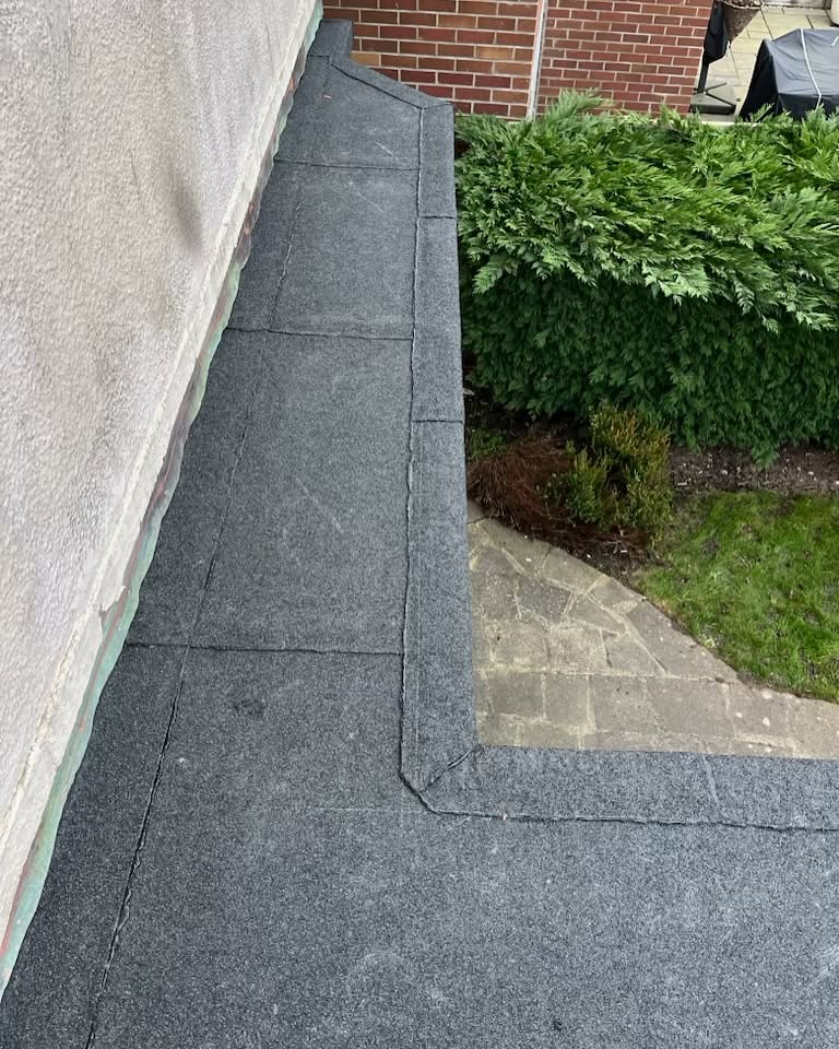 Completed felt flat roof with neat edge trim beside the garden